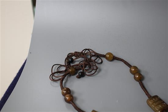 A Chinese hardstone necklace, with carved and inscribed plaque and brown fabric strung beads, plaque 6 x 4.5cm, rectangular beads 2cm a